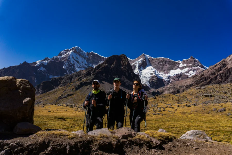 Three hikers standing on the Ausangate Trek surrounded by dramatic snow-covered mountains