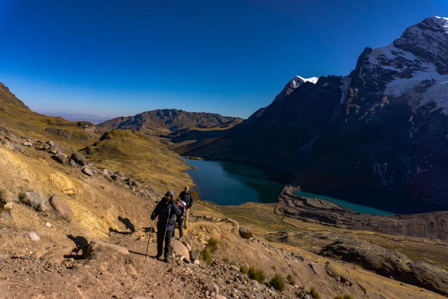 Hikers walking along a rocky mountain trail above a remote lake in the Peruvian Andes