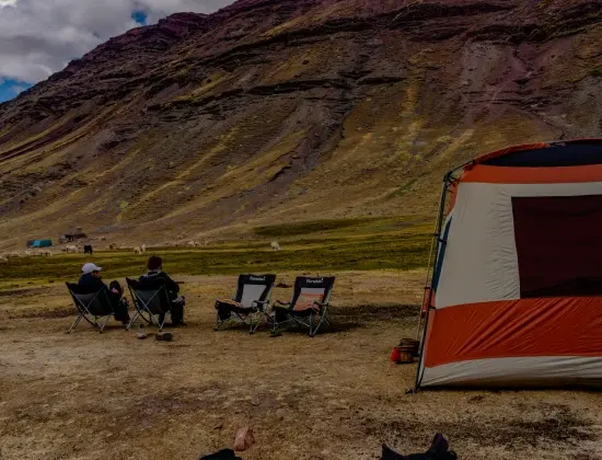 Expedition tent and camping chairs set up in a high-altitude Andean mountain valley.