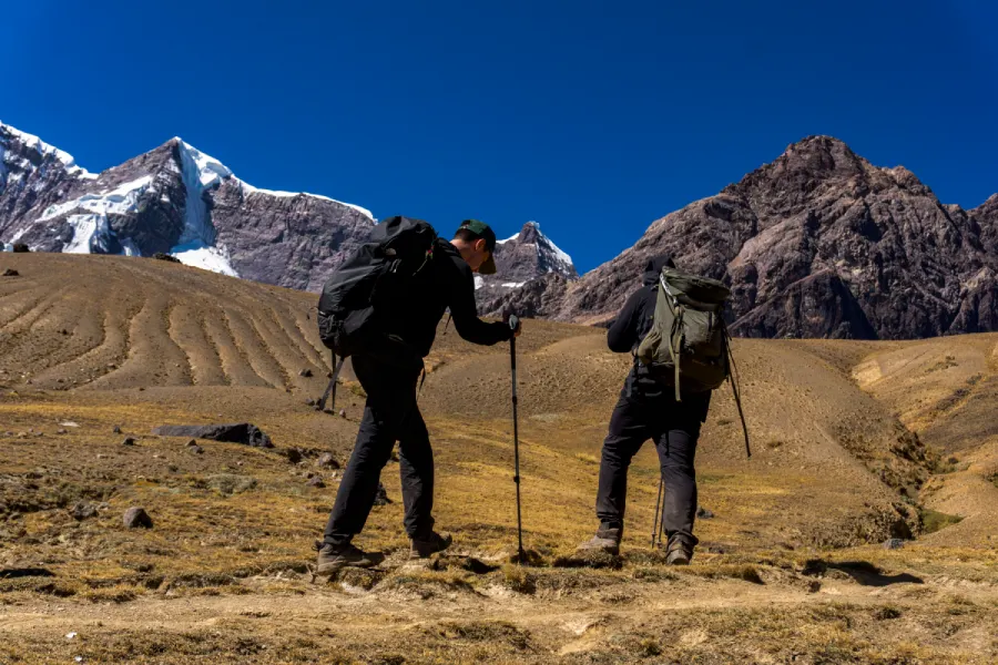 Two hikers wearing mountain footwear and carrying backpacks on a rocky trail in the Peruvian Andes