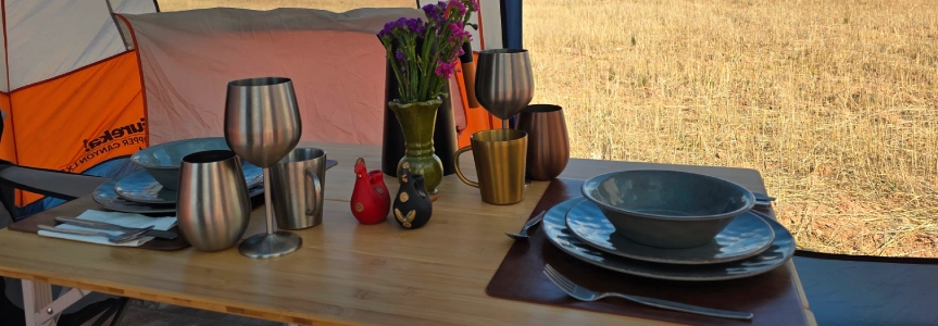 Dining table prepared with plates and drinkware inside a trekking camp tent.