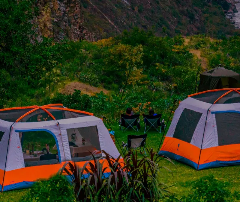 Two glamping tents set up in a green Andean valley beside a river.