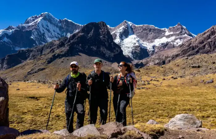 Private vs Group Trekking in Peru: three travelers hiking together beneath snow-capped Andean peaks